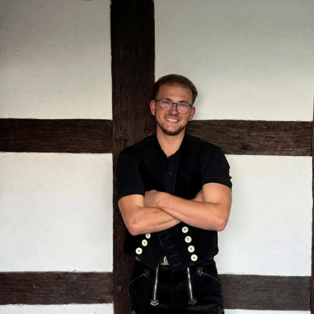 Ein Portraitfoto des Zimmerermeisters Chris Voltermann vor einer Fachwerkwand